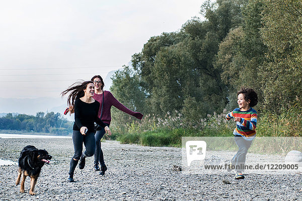 Junge und junge Frauen rennen mit Hund am Flussufer entlang  Calolziocorte  Lombardei  Italien