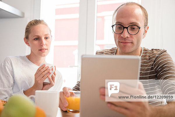 Junge Frau und Freund schauen sich digitales Tablet am Frühstückstisch an