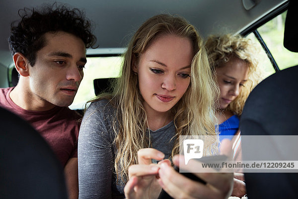 Friends in back seat of car looking at smartphone