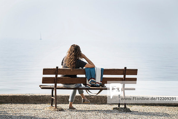Rückansicht einer auf einer Bank sitzenden Frau mit Blick auf den Gardasee  Torri del Benaco  Venetien  Italien  Europa