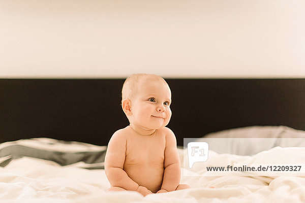 Cute baby girl sitting up on bed looking away