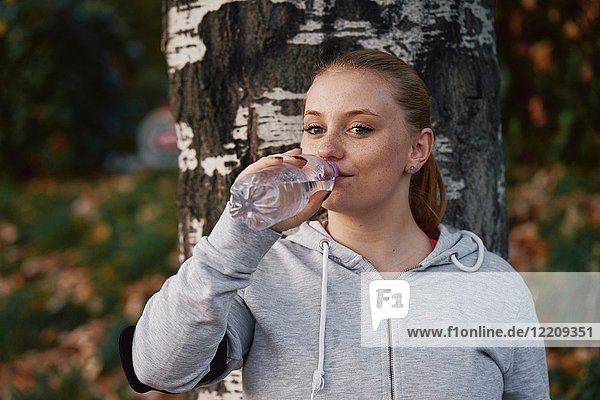 Porträt einer jungen Frau  die im Park trainiert und Flaschenwasser trinkt