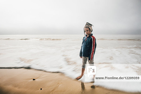 Portrait of boy standing on beach pensive expression