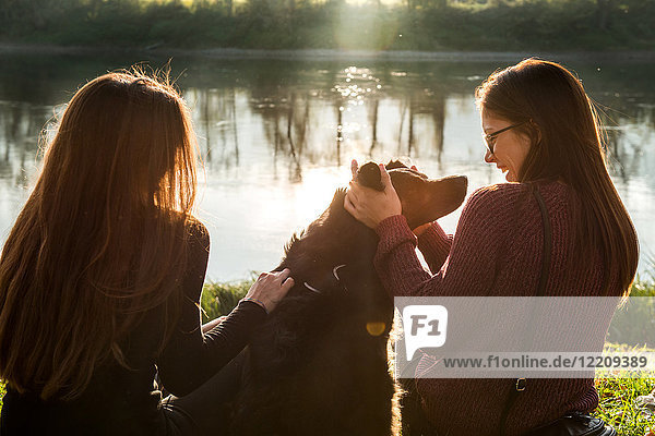 Two young women petting dog on river bank  Calolziocorte  Lombardy  Italy