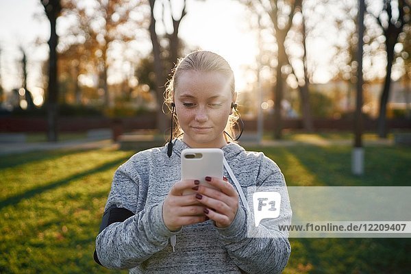 Junge Frau  die im Park trainiert und sich ein Smartphone anschaut