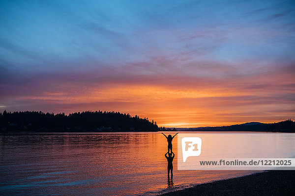 Ehepaar praktiziert Yoga am Strand bei Sonnenuntergang