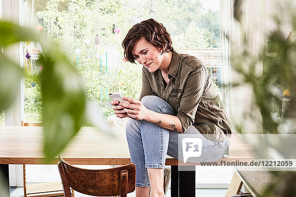 Mittlere erwachsene Frau zu Hause  am Tisch sitzend  mit Smartphone