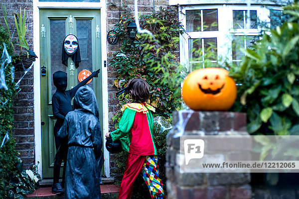 Drei Jungen in Halloween-Kostümen,  an der Tür stehend,  Süßes oder Saures,  Rückansicht