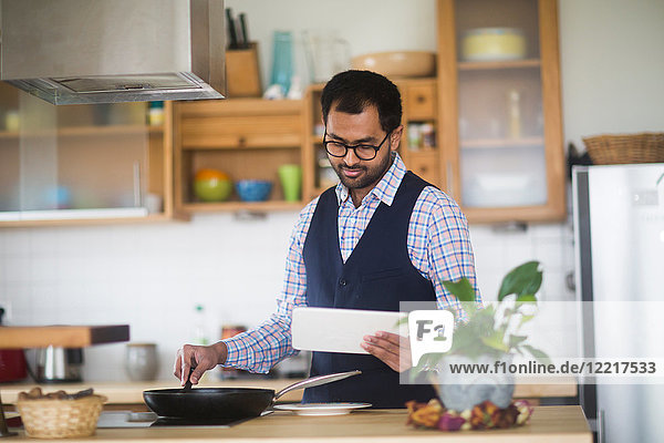Mann kocht  während er zu Hause ein digitales Tablet benutzt