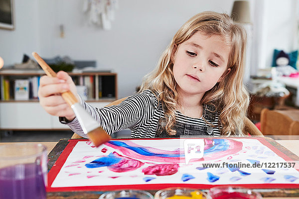 Young girl sitting at table  painting picture
