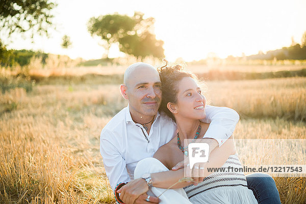 Paar sitzt auf dem Feld und umarmt sich