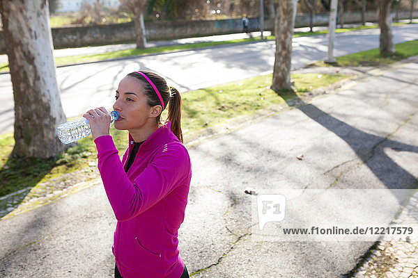 Junge Frau auf der Straße trinkt Wasser aus Wasserflasche