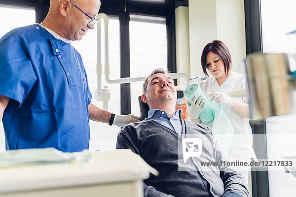 Männlicher Patient auf Zahnarztstuhl  neben ihm stehender Zahnarzt