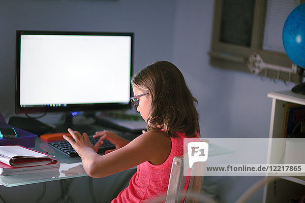 Young girl sitting at desk  doing homework  using computer
