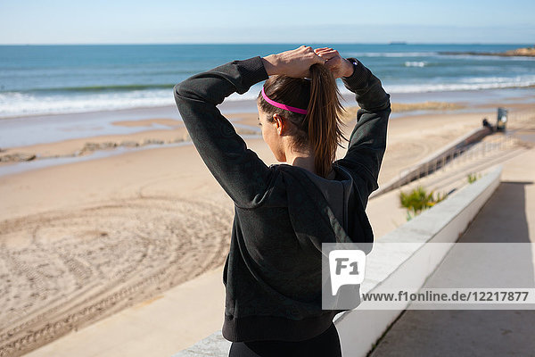 Rückansicht einer jungen Frau am Strand beim Binden der Haare am Pferdeschwanz  Carcavelos  Lissabon  Portugal  Europa