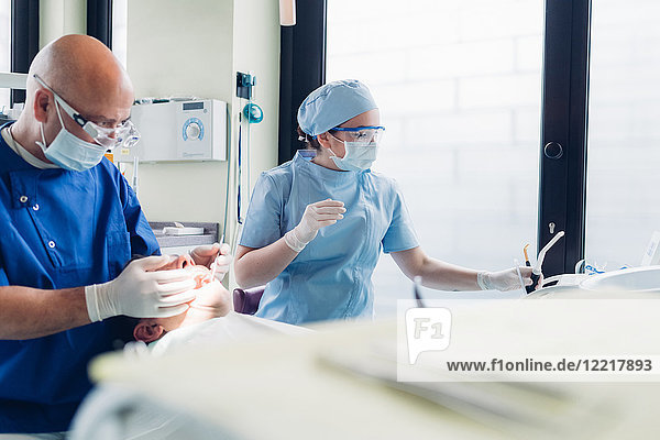 Zahnarzt und Zahnarzthelferin  die einen zahnärztlichen Eingriff an einem männlichen Patienten vornehmen  Nahaufnahme