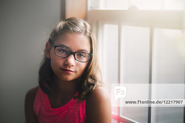 Portrait of young girl wearing glasses  standing beside window  pensive expression