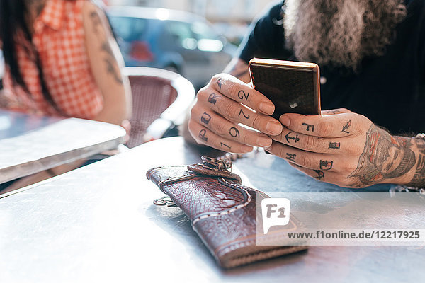 Älterer Hipster-Mann benutzt Smartphone im Straßencafé  Nahaufnahme der tätowierten Hand
