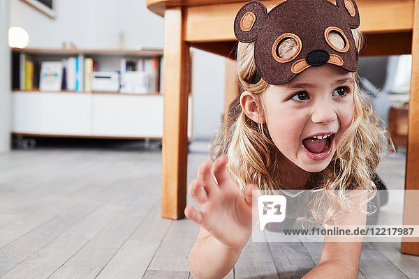 Young girl crawling under table  wearing bear mask  laughing