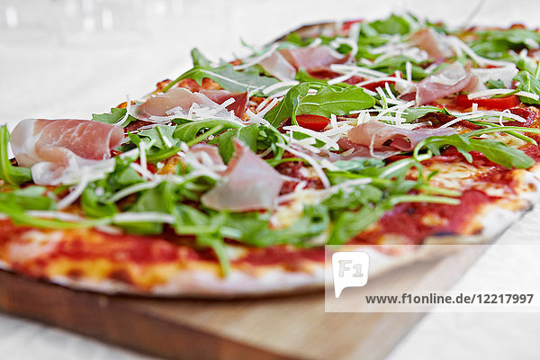 Fresh pizza with rocket and parma ham on chopping board