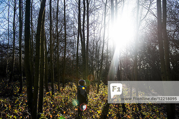 Junge steht im Wald und schaut durch Bäume auf die Sonne