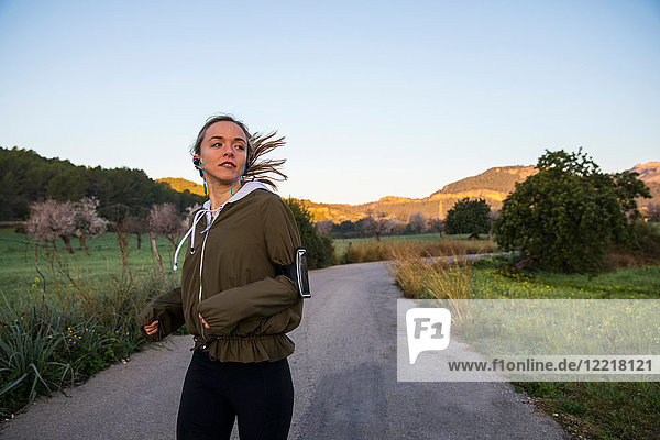 Junge Frau läuft entlang einer Landstraße und trägt einen Aktivitäts-Tracker