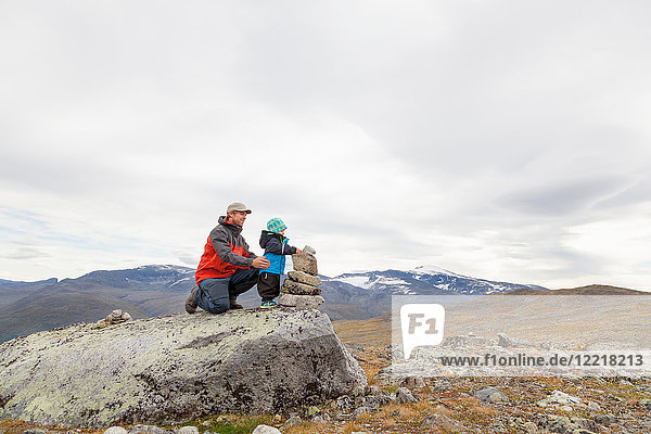 Male hiker with son building cairn in mountain landscape  Jotunheimen National Park  Lom  Oppland  Norway
