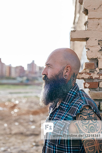 Tätowierter reifer männlicher Hipster an der Wand eines abgerissenen Gebäudes