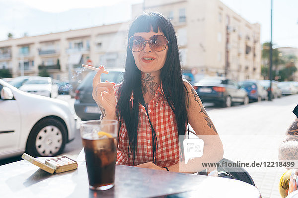Reife Hipsterin raucht Zigarette im Straßencafé