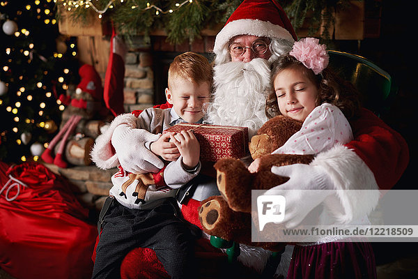 Mädchen und Junge besuchen den Weihnachtsmann und halten Geschenke in der Hand
