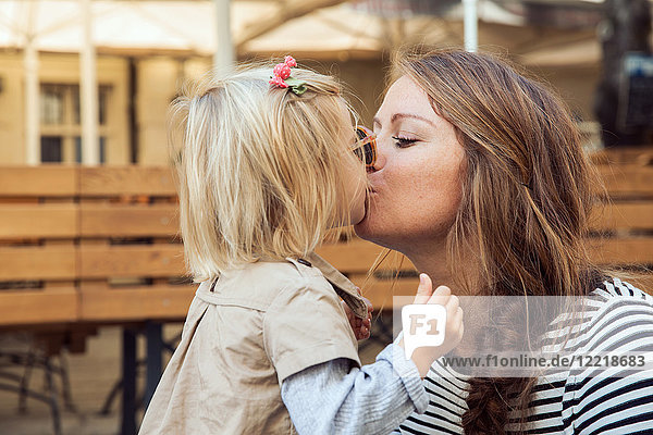 Mutter küsst Kleinkind-Tochter auf Parkbank