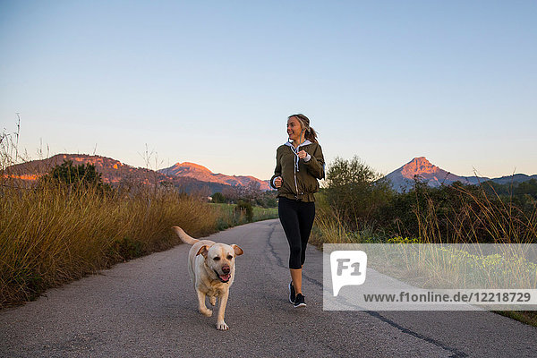 Junge Frau rennt mit Haushund die Landstraße entlang