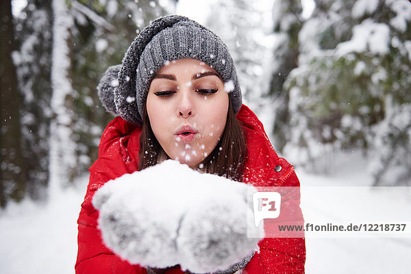 Young woman blowing snowflakes off hands