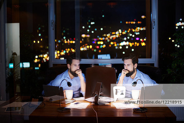 Young businessman at office desk looking at computer at night  mirror image