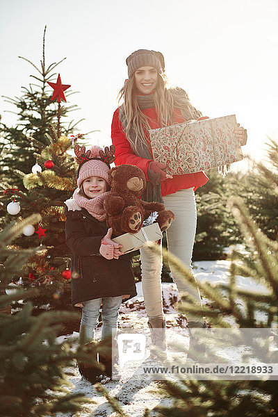 Mädchen und Mutter im Weihnachtsbaumwald mit Weihnachtsgeschenken  Portrait
