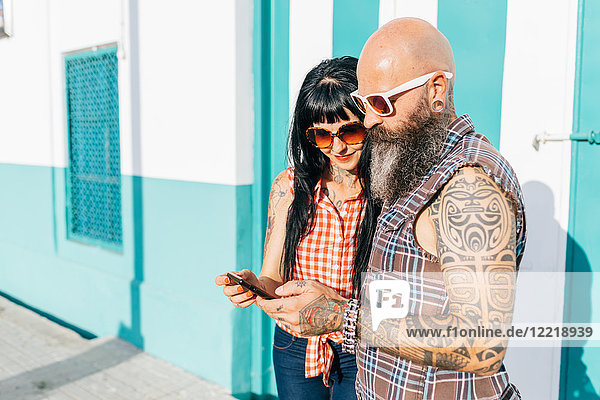 Mature hipster couple looking at smartphone on sidewalk