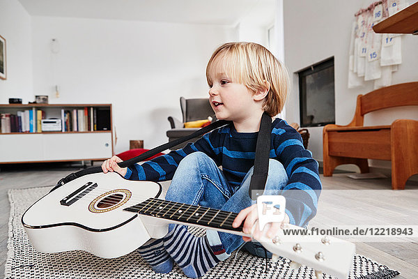 Junger Junge sitzt mit Gitarre um den Hals
