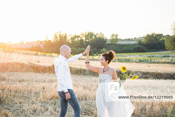 Heterosexuelles Paar tanzt auf Feldern  Frau hält Sonnenblumen in der Hand