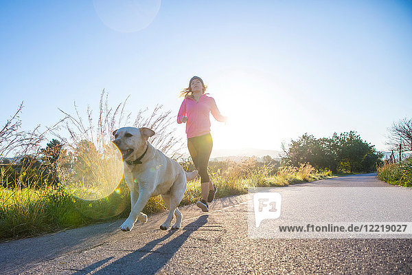 Junge Frau rennt mit einem Haushund entlang einer Landstraße  niedriger Blickwinkel