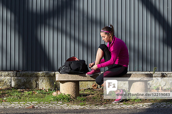Junge Frau auf Bank bindet Schnürsenkel am Trainingsschuh