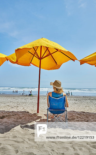 Rückansicht einer Touristin  die unter einem Sonnenschirm am Strand sitzt  Camana  Arequipa  Peru