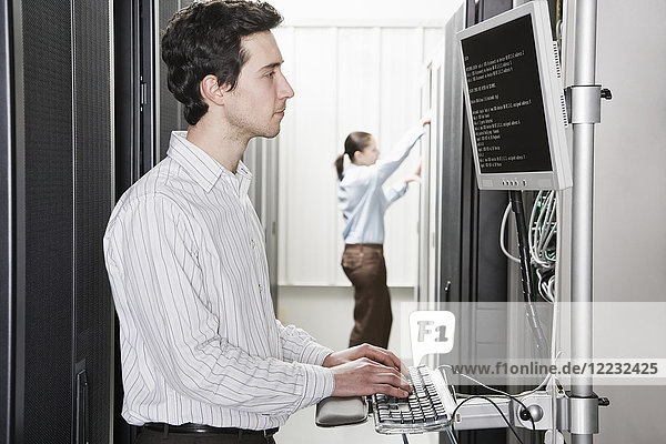 A male computer technician standing in an aisle of racks of servers in a computer server farm