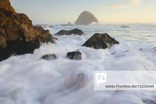 Meereslandschaft mit brechenden Wellen über Felsen in der Abenddämmerung.