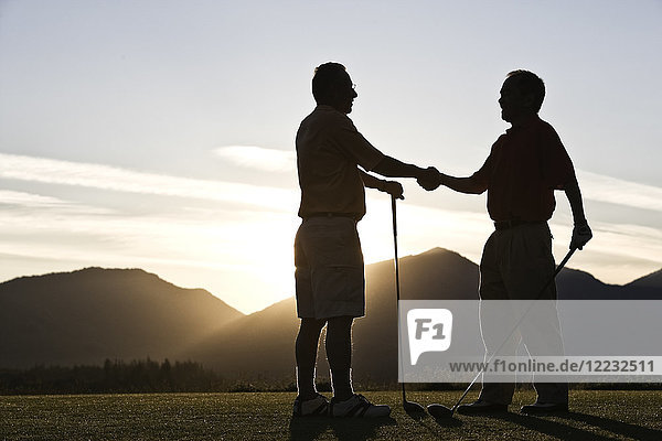 Zwei ältere Freunde nähern sich bei Sonnenaufgang dem ersten Abschlag eines Golfplatzes.