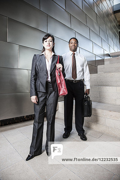 Schwarzer Geschäftsmann und hispanische Geschäftsfrau in der Lobby eines großen Bürogebäudes.