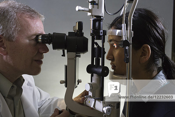 Kaukasischer Mann Augenarzt  der ein Spaltlampentanometer am Auge eines Patienten verwendet.