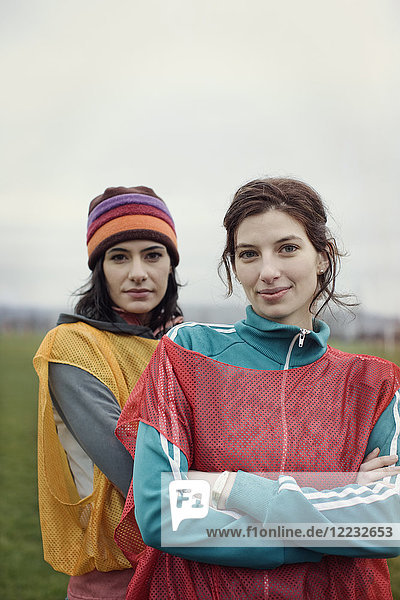Porträt von zwei kaukasischen Frauen in Sportkleidung mit den Startnummern der gegnerischen Mannschaften und Wollmützen nebeneinander.