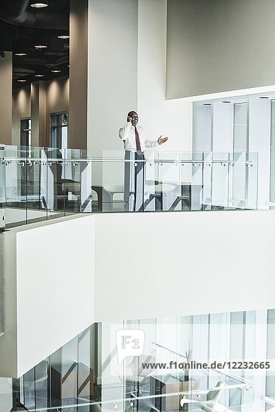 Schwarzer Geschäftsmann am Telefon  der in der Lobby eines großen Geschäftszentrums steht.