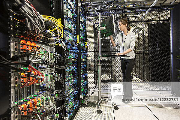 Caucasian woman technician doing diagnostic tests on computer servers in a server farm.