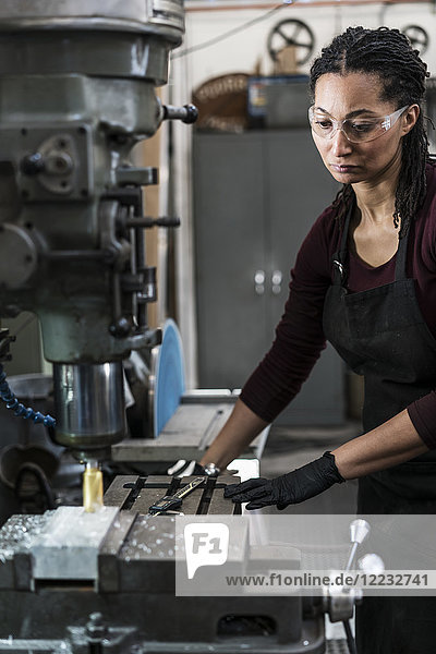 Frau mit Schutzbrille steht in einer Metallwerkstatt und arbeitet an einer Maschine.